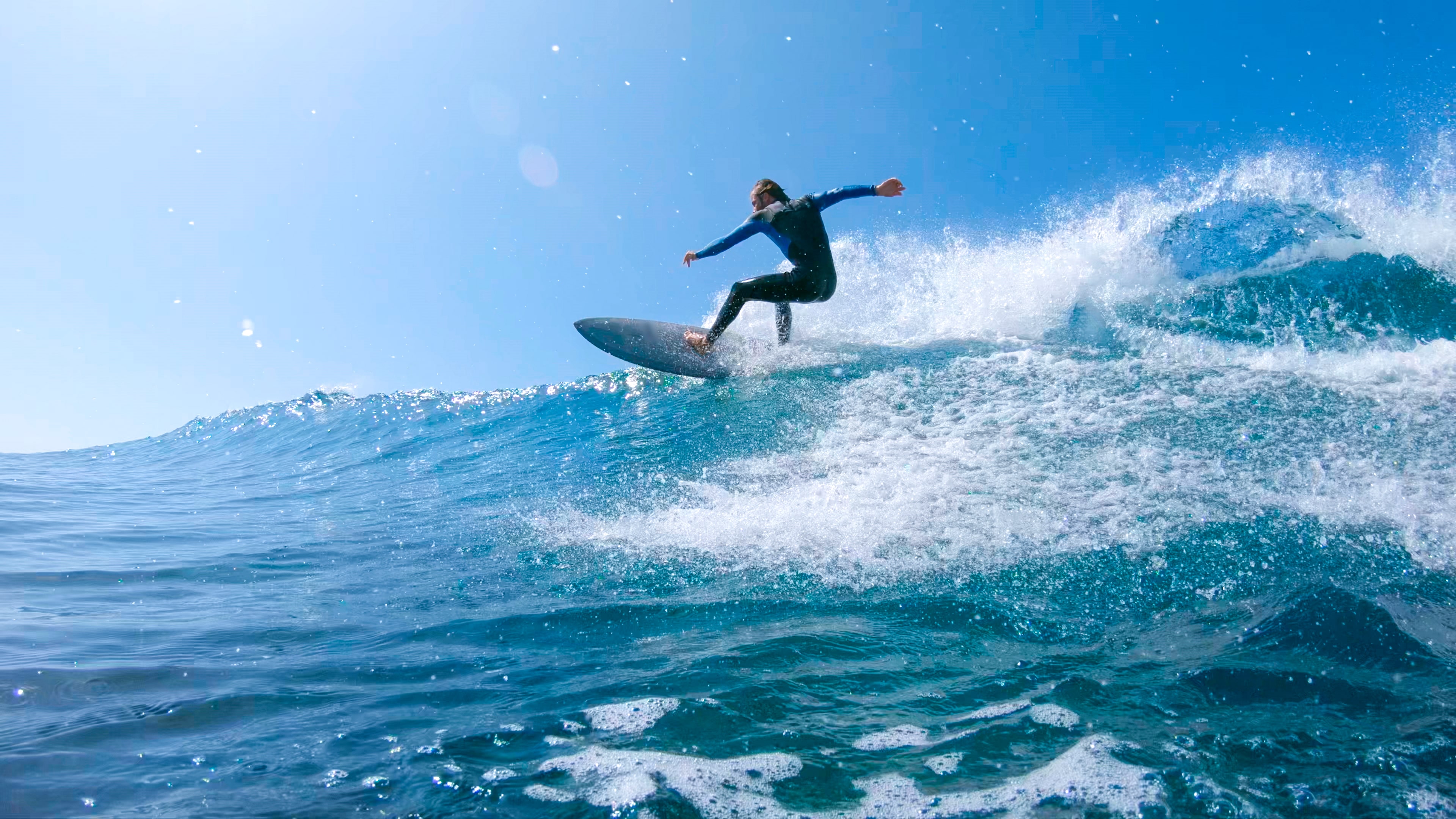 Surfeur réalisant une manœuvre sur une grande vague bleue sous un ciel ensoleillé à Fuerteventura.